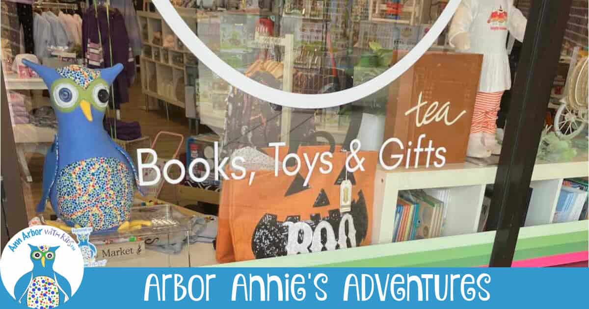 Arbor Annie's Adventures - A Stuffed Arbor Annie sits in the My Urban Toddler shop window behind glass that says Books, Toys, & Gifts