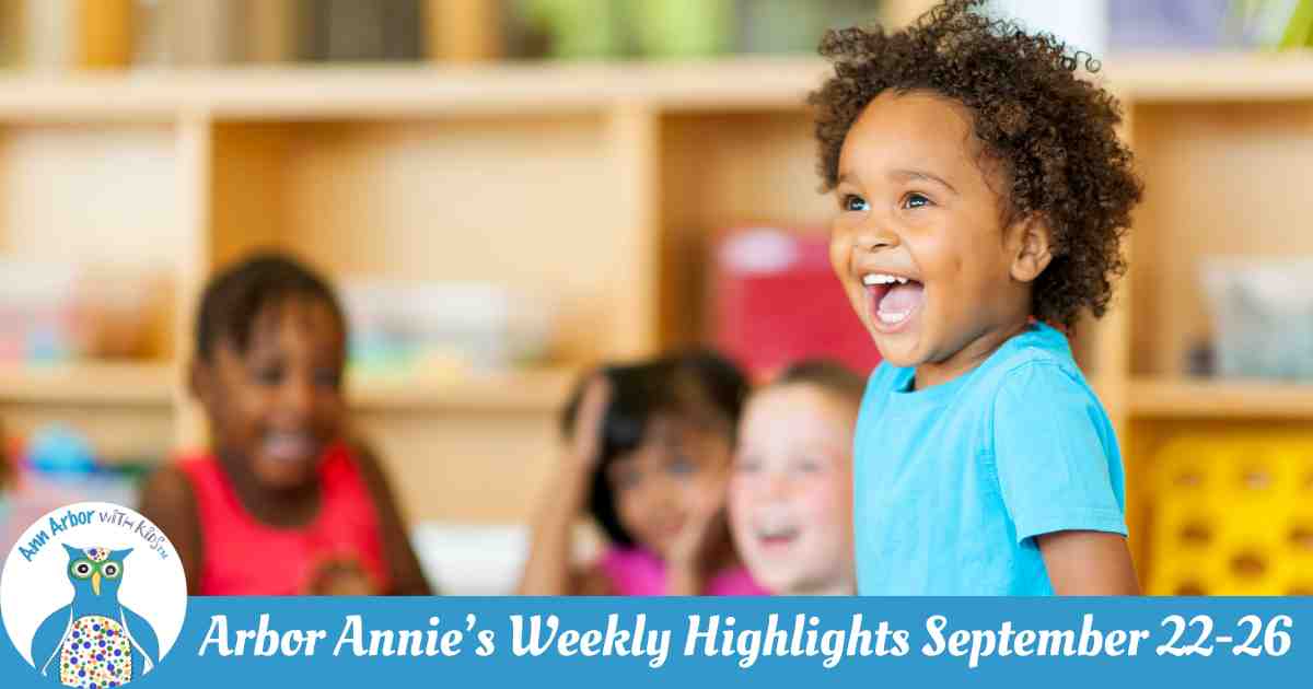 Arbor Annie's Weekly Highlights - September 22-26 - A young preschooler in focus is standing & laughing in a classroom while other slightly older children are sitting behind him, smiling, but out of focus