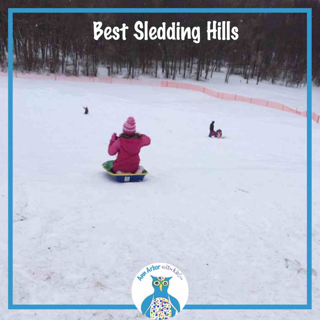 Ann Arbor's Best Sledding Hills - the view of Rolling Hills sledding hill from the top with a girl in a pink coat & hat on a green sled going down