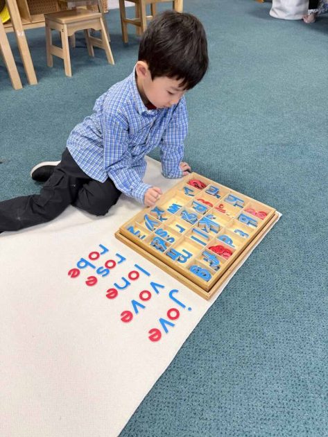 A boy sits on the floor and forms words from letter cutouts