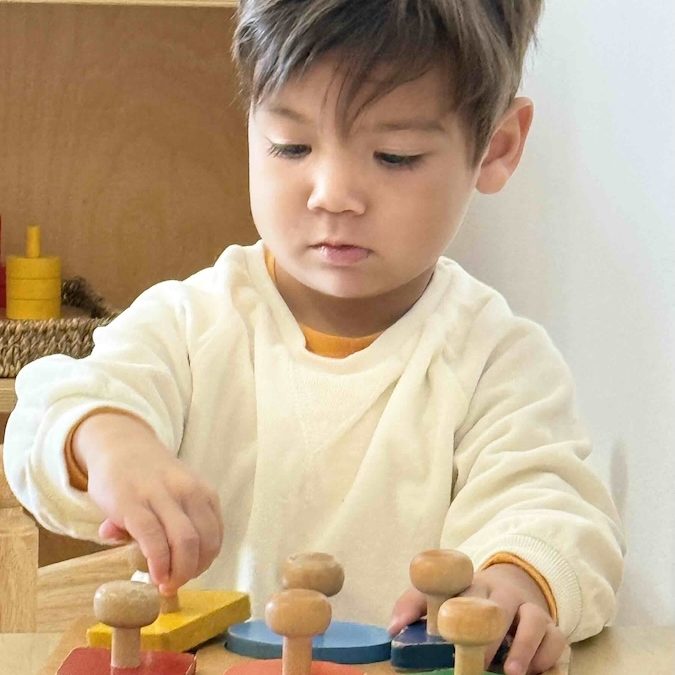 Daycroft School - a boy works on a wooden puzzle with large pieces on handles.