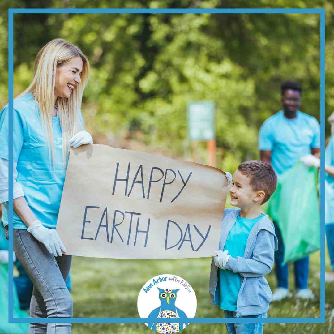 Earth Day - a mom & child outside holding a Happy Earth Day sign. Volunteers in back collect trash
