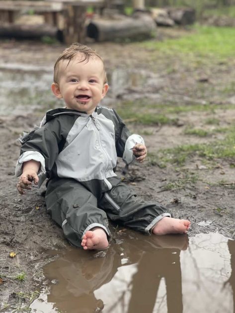 Green Apple Garden Lower School - A baby sits outside in front of a puddle
