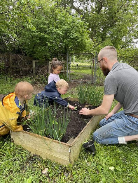 Green Apple Garden Lower School - a man guides toddlers working in a raised planter bed