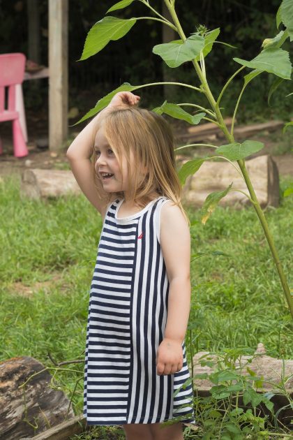 Child in sundress measures themself against a sunflower stalk