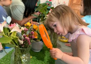 Manzanitas - Girl Examining flowers through a giant magnifying glass