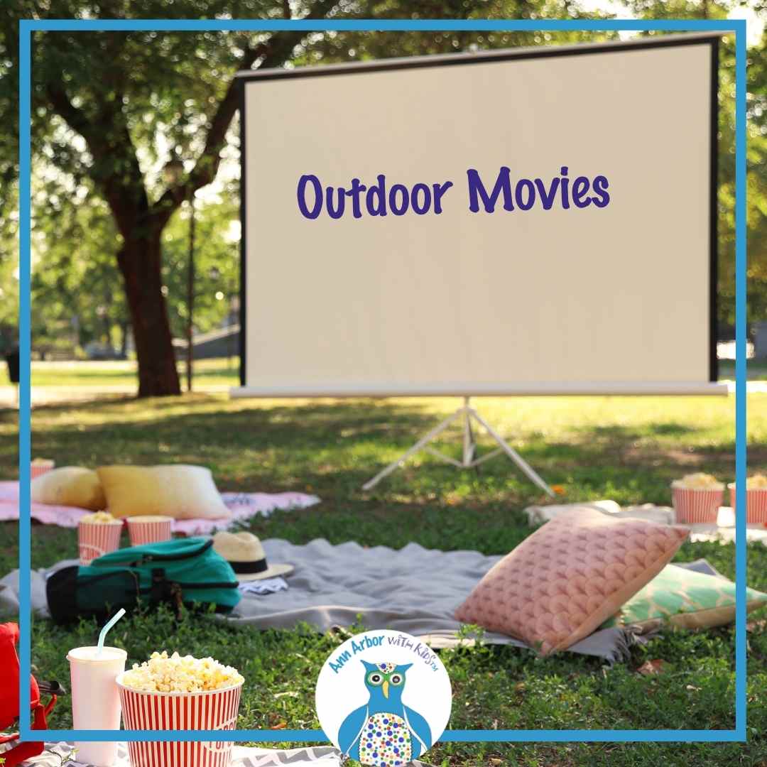 Outdoor Movies - a movie screen setup in a park with blankets, pillows, drinks & popcorn spread on the grass