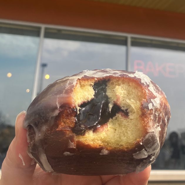 Paczki with a bite out of it showing the blueberry filling with the windows of Dimo's Deli & Donuts behind it
