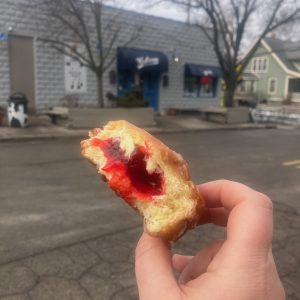 Paczki with bite out of it showing the raspberry filling inside. Photo is taken across the street from Washtenaw Dairy visible in the background