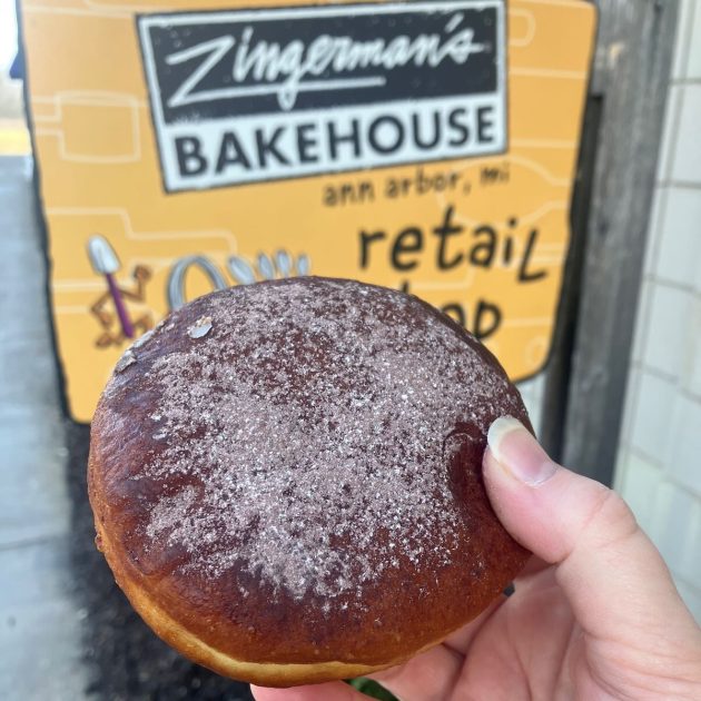 Paczki coated in cinnamon in front of Zingerman's Bakehouse sign for the retail shop