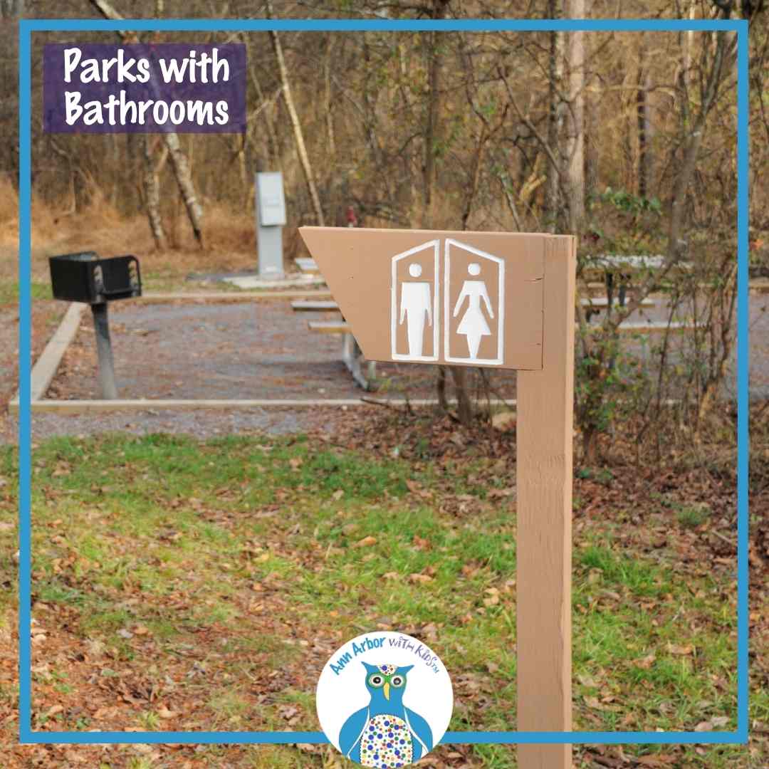 Parks with Bathrooms - a sign with men's & women's restroom signs in front of a mulch area with park grill and picnic tables
