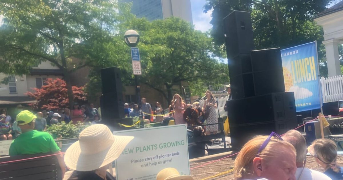Sonic Lunch - photo from the crowd of Sonic Lunch performers on stage - taken from the side with the LUNCH portion of the sign behind the stage visible