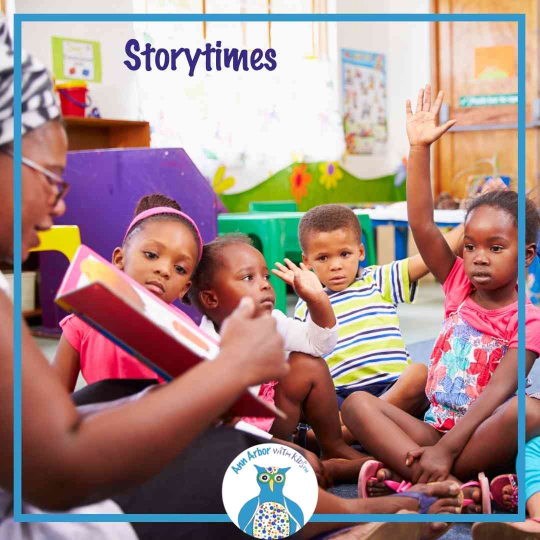 Ann Arbor Story times -A teacher reads from a picture book to a group of preschoolers with one raising their hand