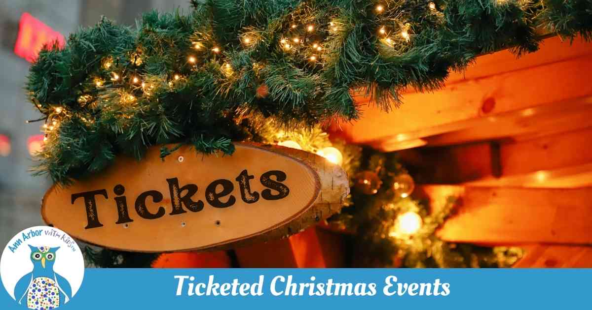 Ticketed Christmas Events - A wooden booth trimmed with greenery, lights, and a bow with wooden sign that says Tickets