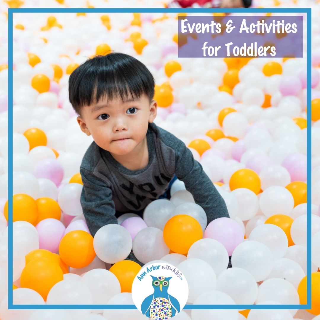 Events & Activities for Toddlers - a toddler in a giant ball pit with white, yellow, clear, & pink balls