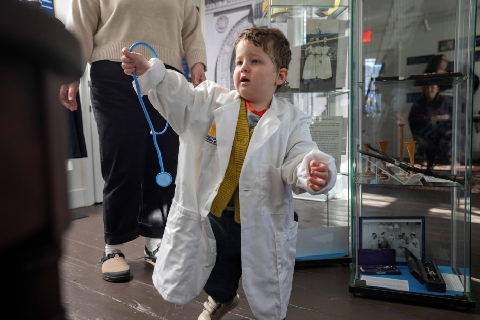 A toddler boy tries on a UM Medicine lab coat and stethoscope